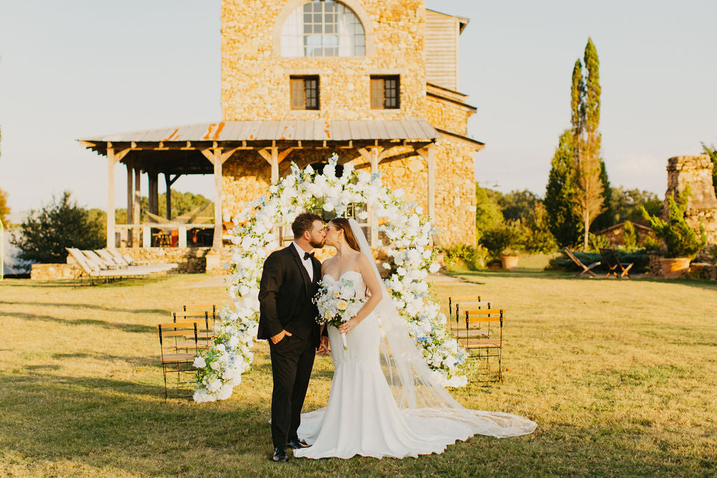 A wedding couple kissing in front of the Anastasia Arch while holding the Anastasia bridal bouquet to match perfectly.