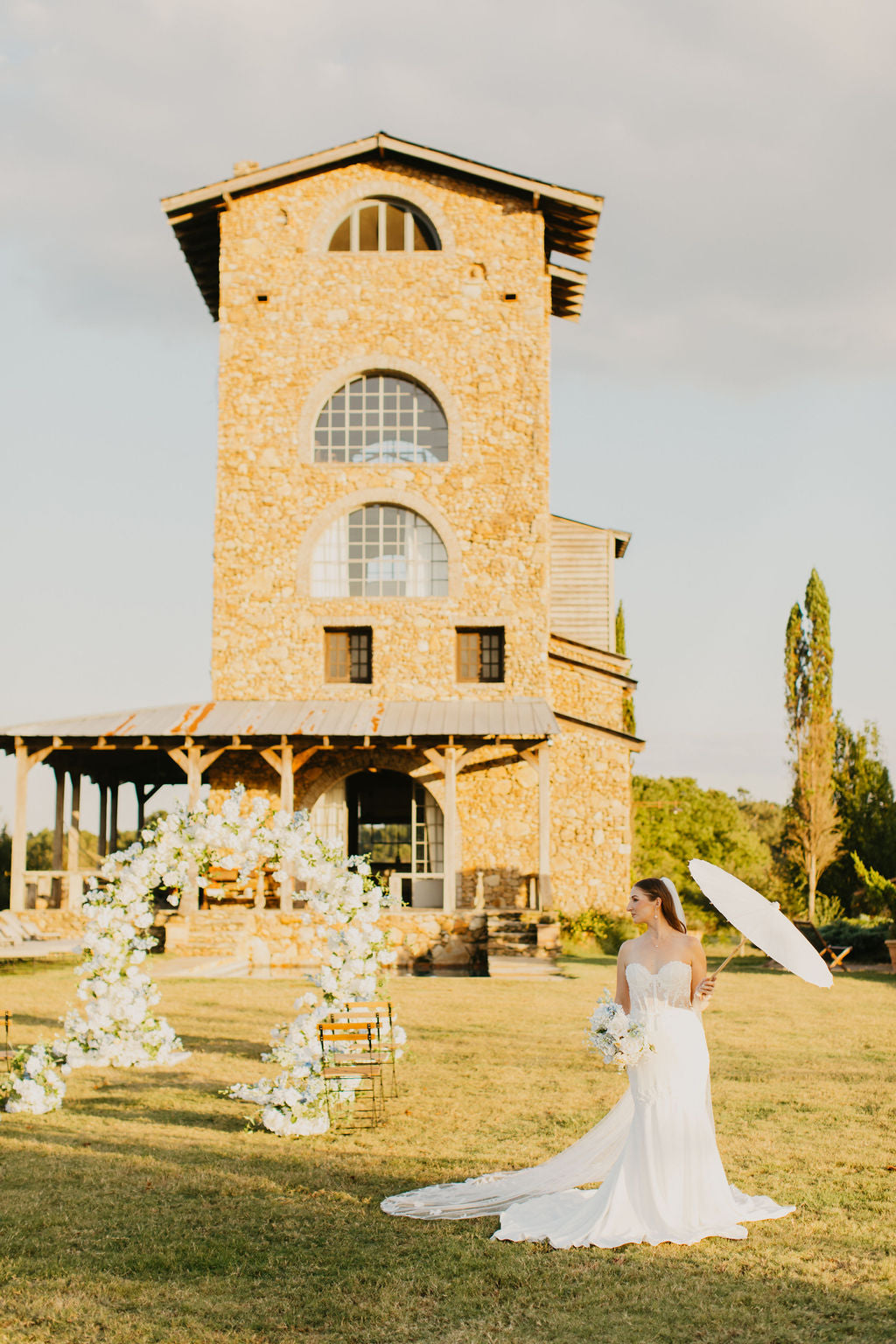 Bride standing by the Anastasia arch, framed by soft white roses and pastel florals in a graceful and timeless wedding setting.