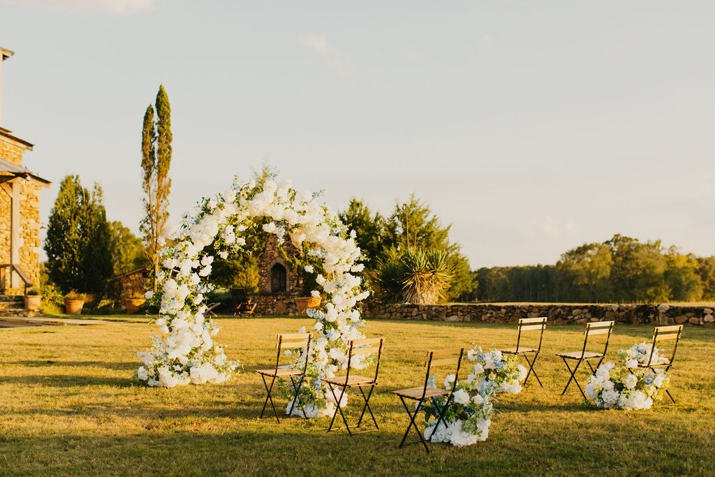 The Anastasia Arch set up outdoors, highlighting airy florals in yellow, blue, and white tones against a bright ceremony backdrop.