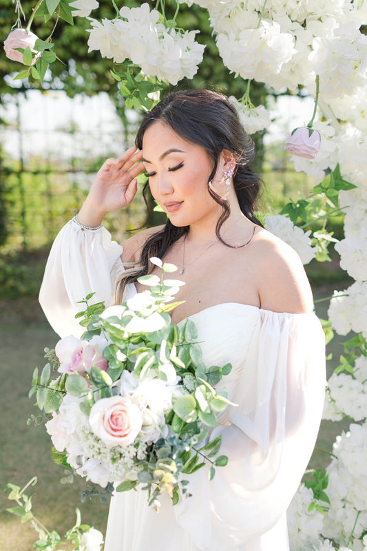 Bride holding the Belle Bridal Bouquet, highlighting its romantic blend of soft white blooms and delicate greenery against a flowing gown.