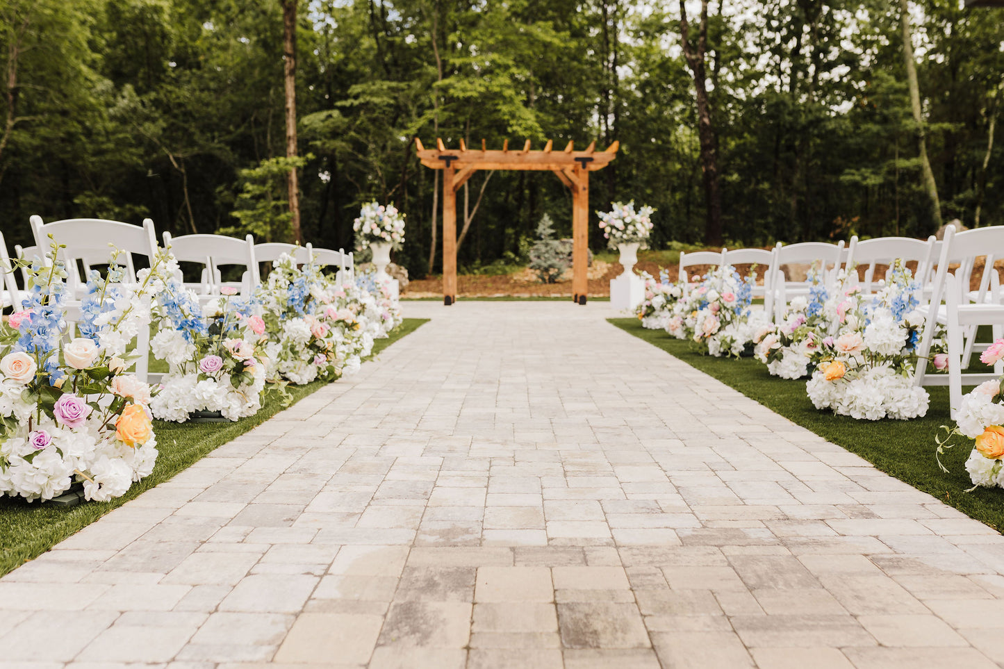 Ceremony space filled with wildflower aisle bouquets and a pair of colorful bloom filled urns on pedestals.