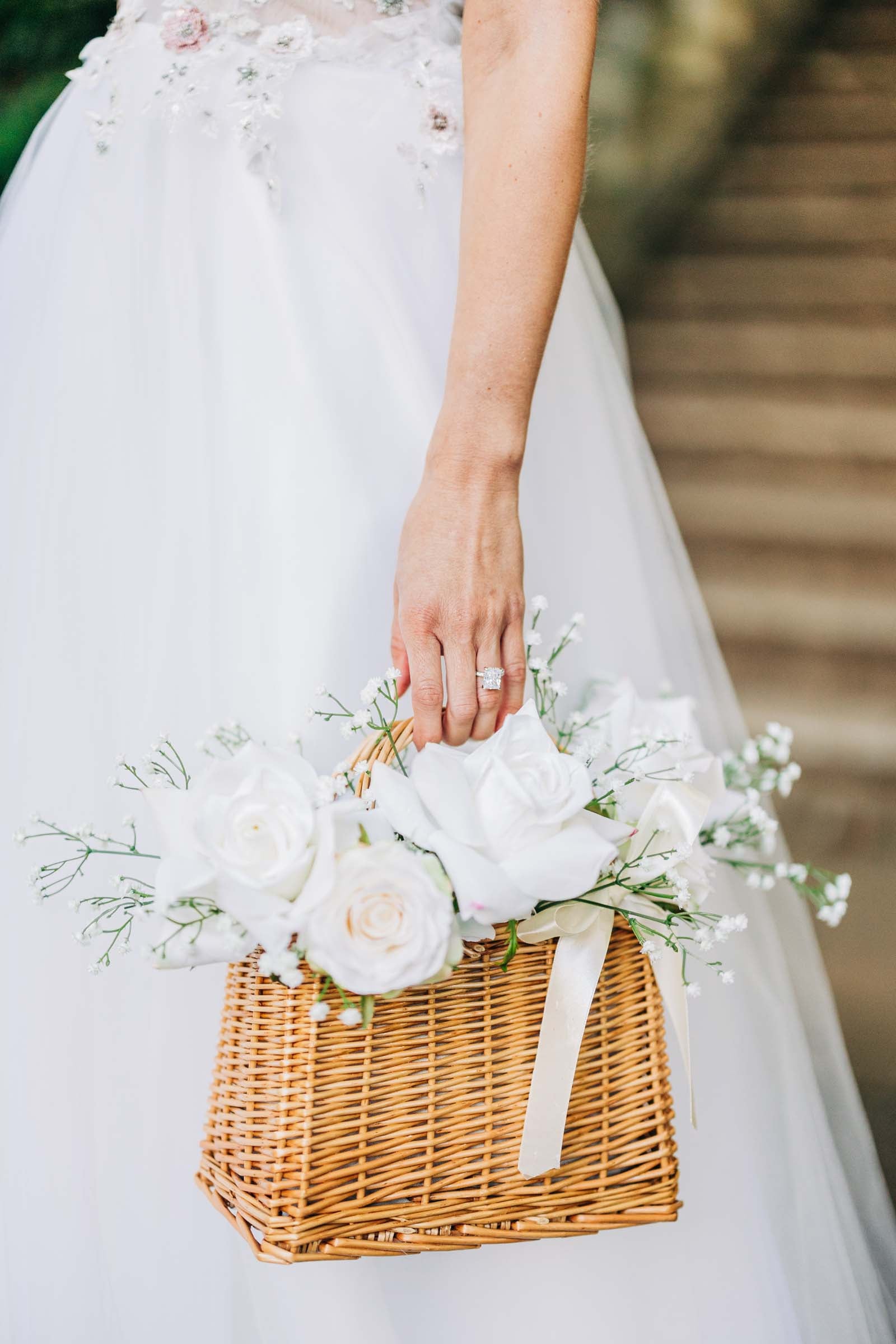 Wicker flower girl basket filled with soft faux florals in white, blush, and greenery- perfect for tossing petals or carrying down the aisle.
