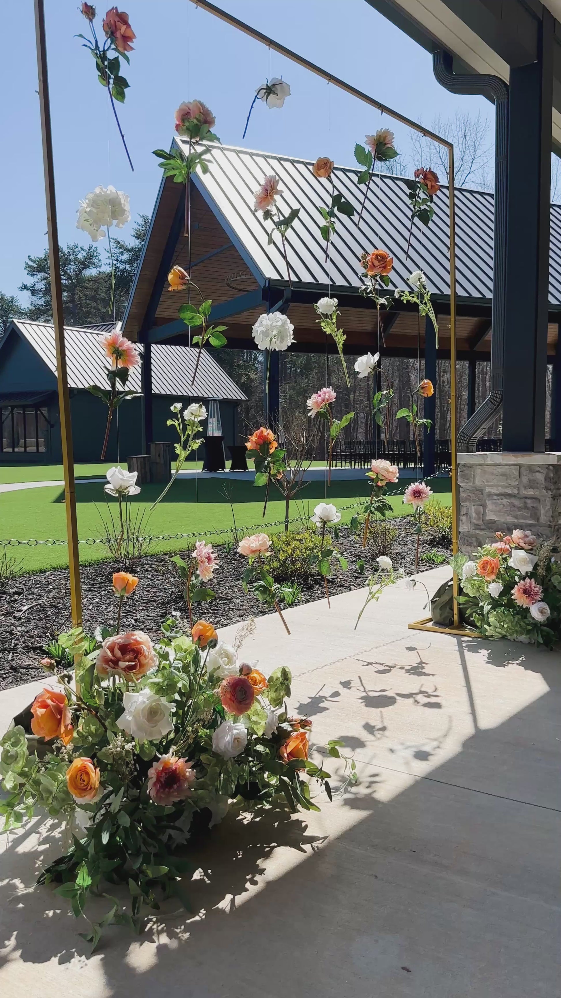 Elevated hanging florals on an elegant gold frame with two bouquets resting on the ground.